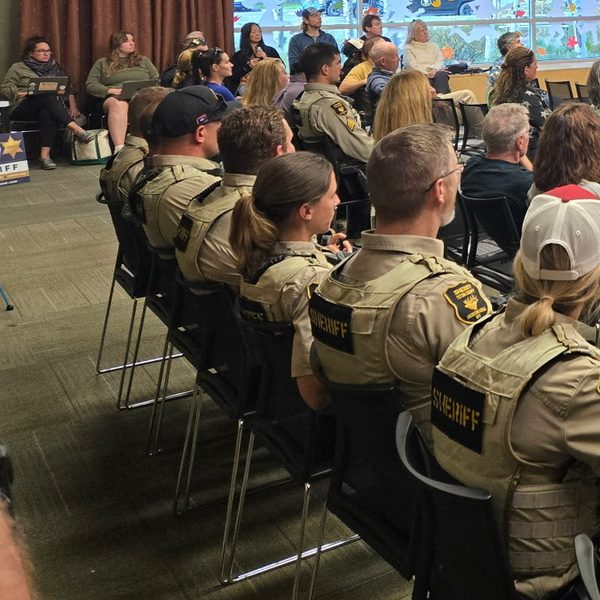 Thumbnail of Exhibit H, deputies in SHERIFF vests seated at the forum while Snow speaks in uniform.